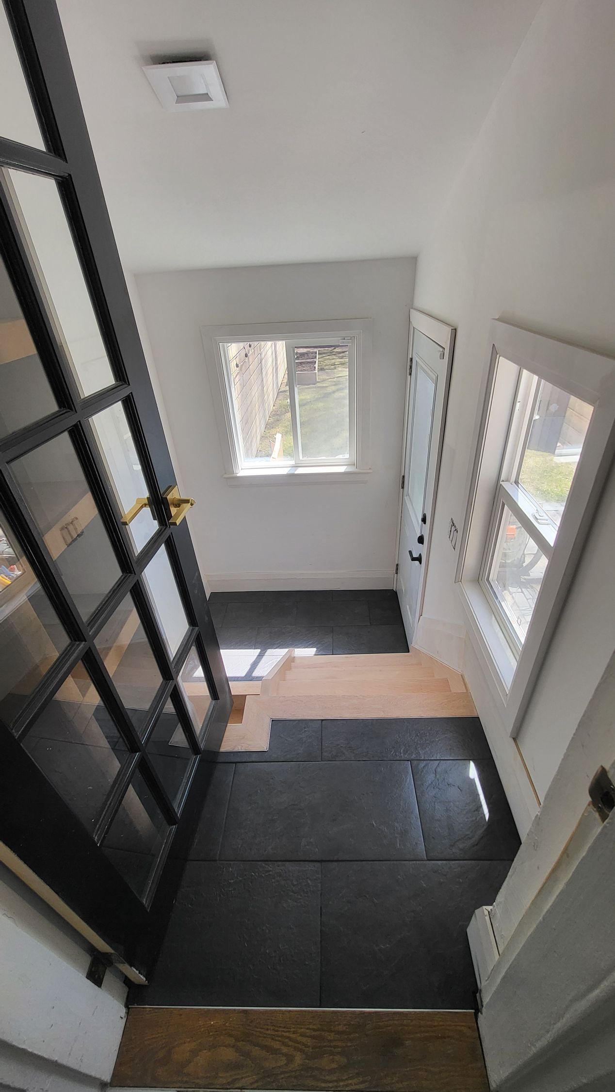 Narrow hallway with black door, window, and partially installed dark flooring.