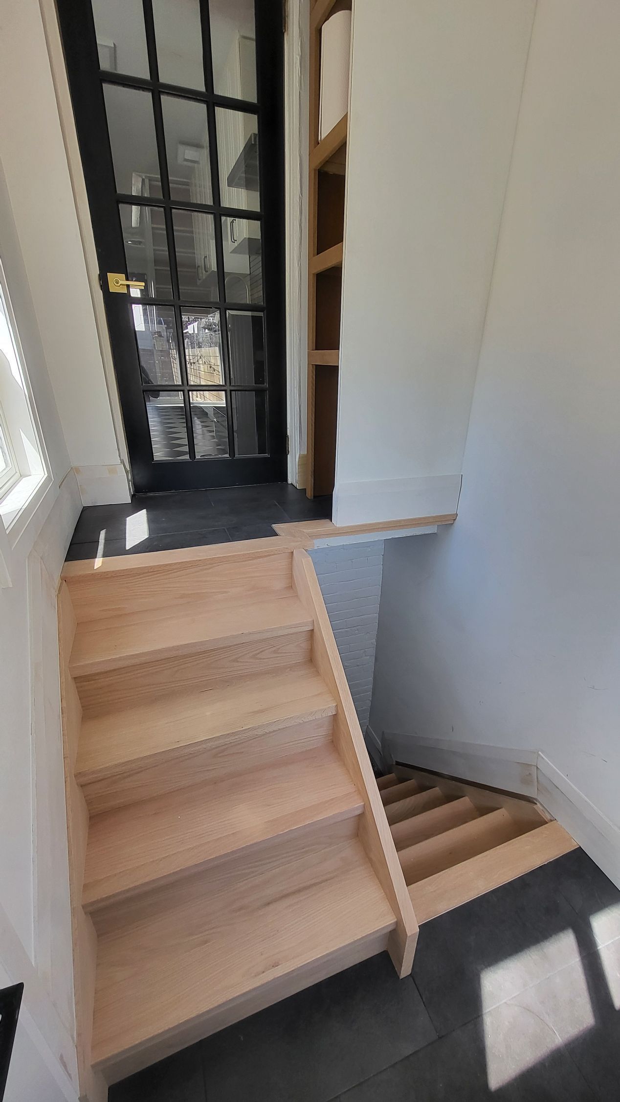 Wooden stairs lead up to a doorway. Small flight of stairs on right. Black floor. White walls.