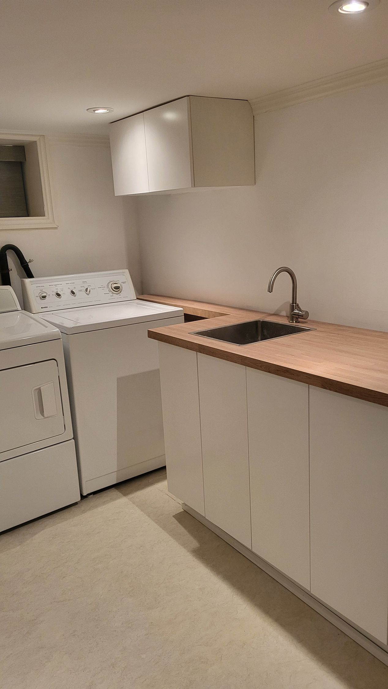 Laundry room with white cabinets, wood countertop, sink, and washing machine.