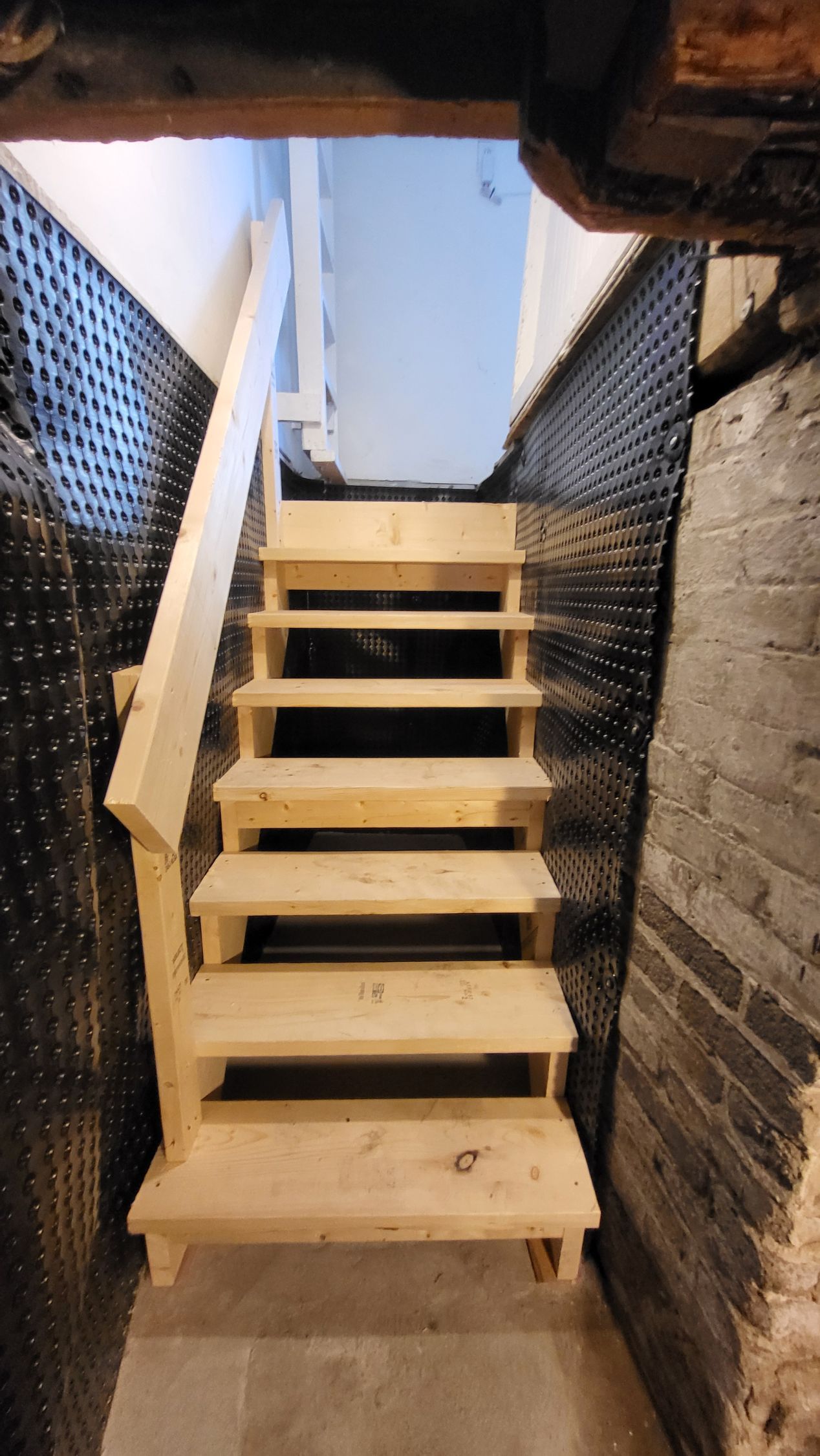 Wooden staircase leading upwards in a basement setting, with handrail on the left.