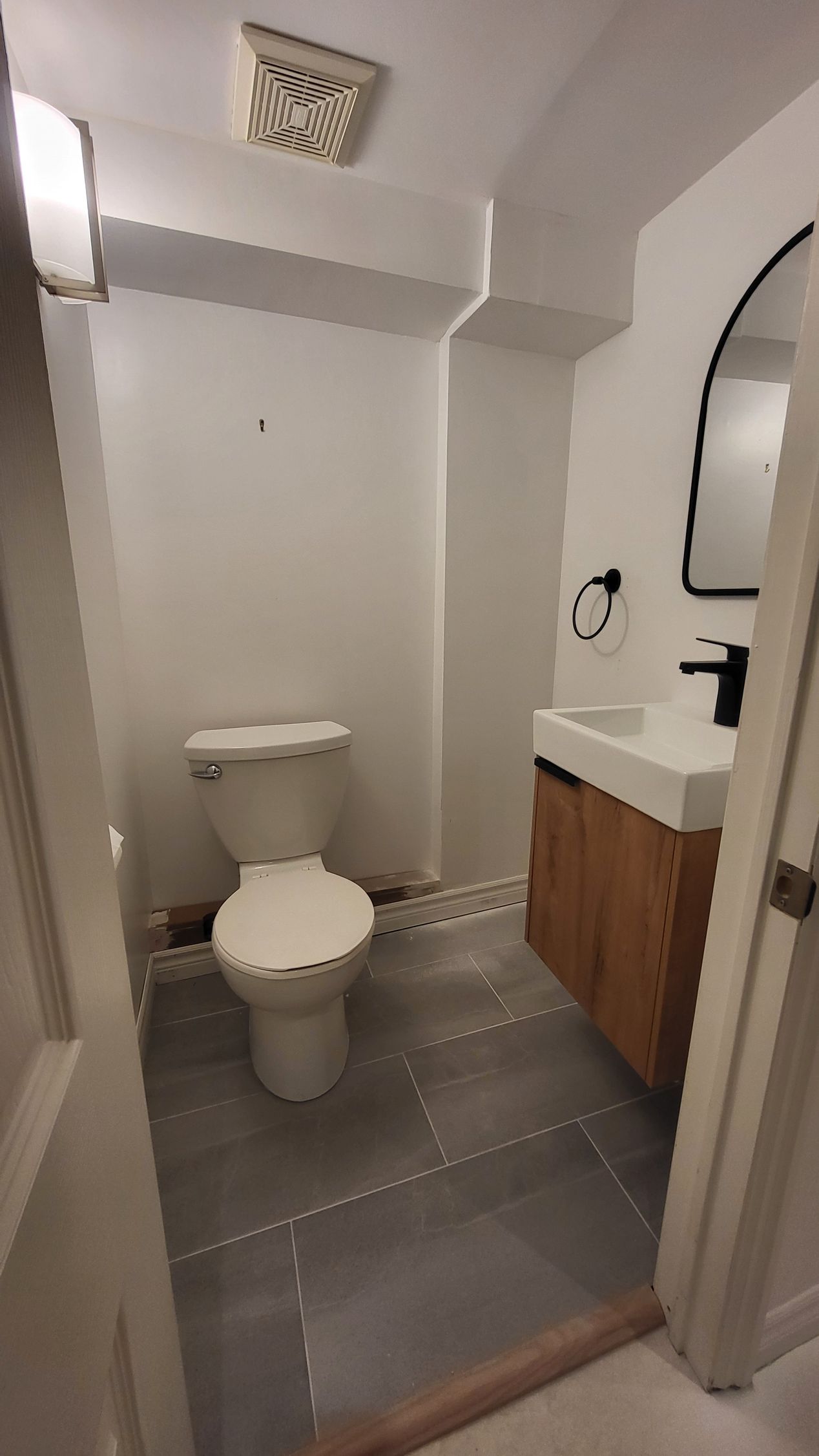 Small bathroom with white walls, toilet, vanity with wood cabinet and gray tile floor.