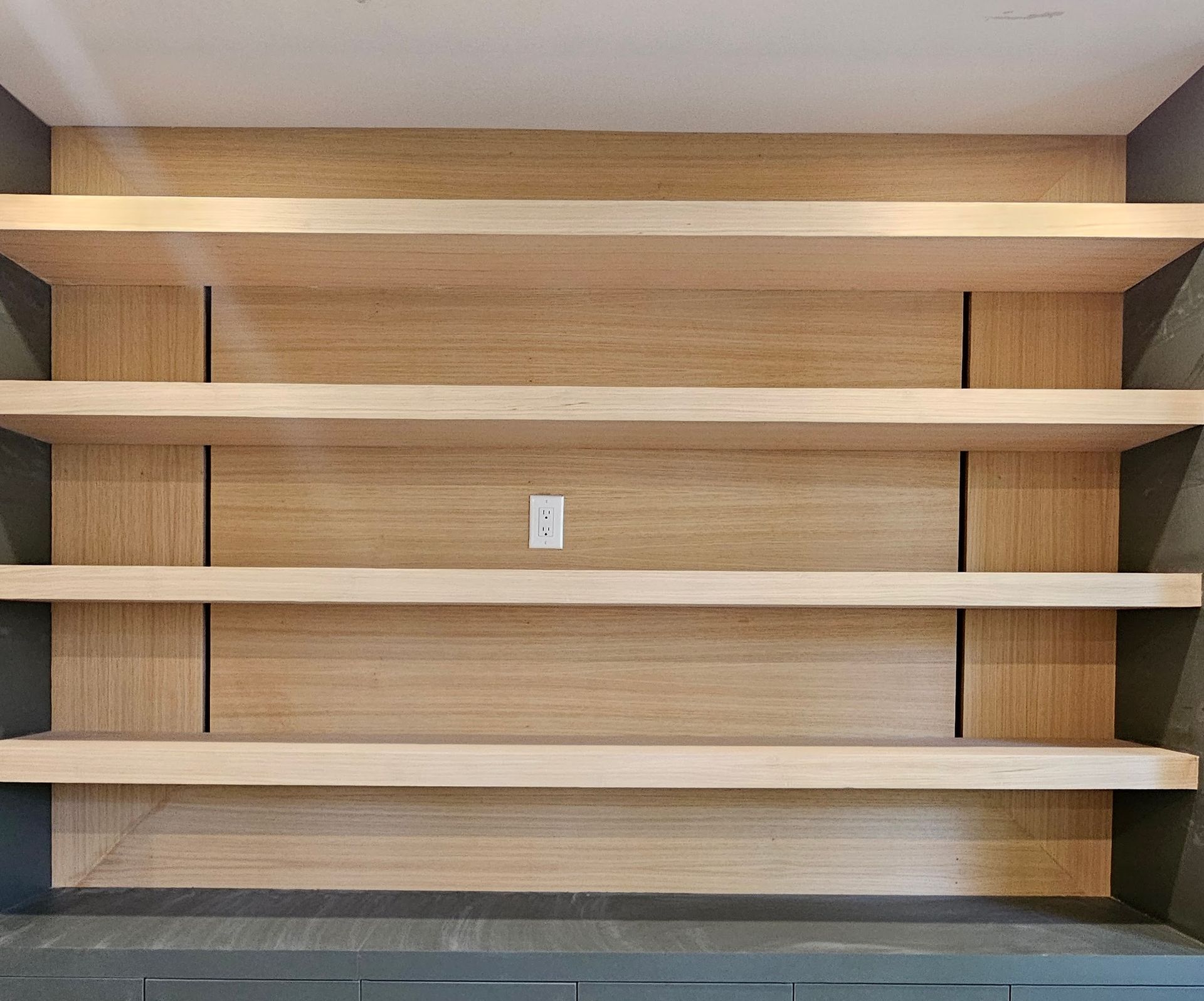 Light wood shelves built into a wall, with dark gray surrounding, and an electrical outlet.