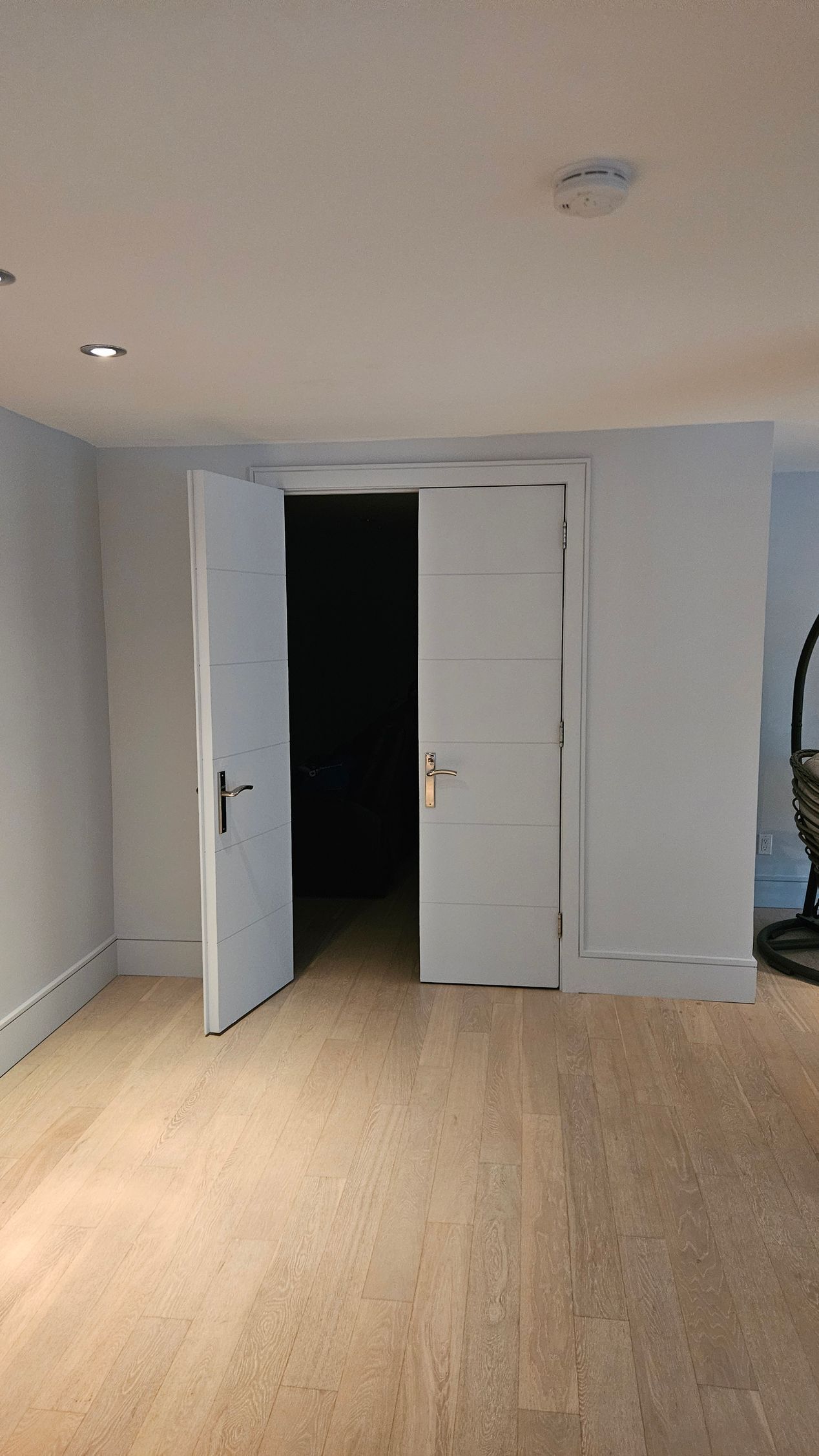 Two open white doors leading to a dark room, situated between pale blue walls in a room with light brown carpet.
