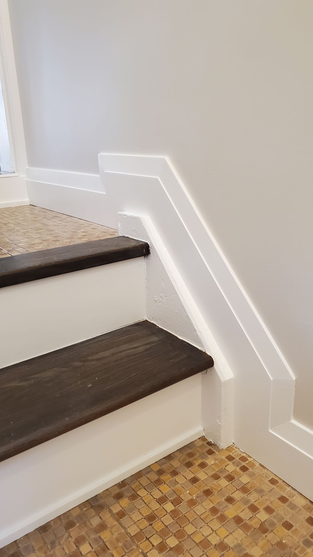 Staircase with dark wood steps and white risers, leading upwards next to a white wall with molding.