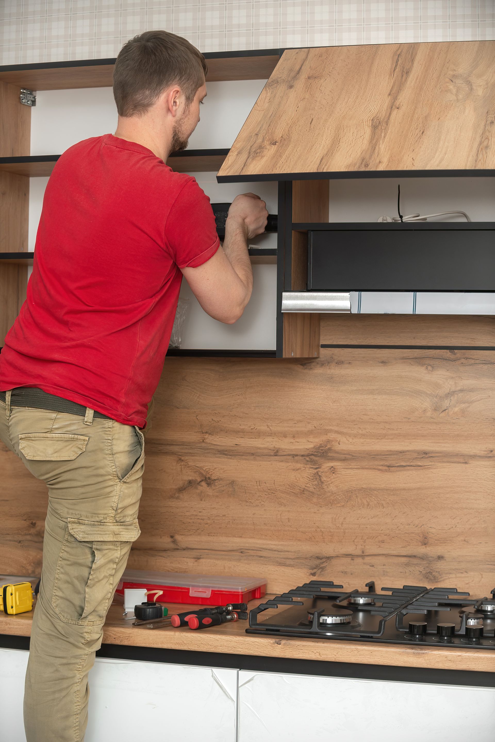 A man in a red shirt is working on a kitchen cabinet.