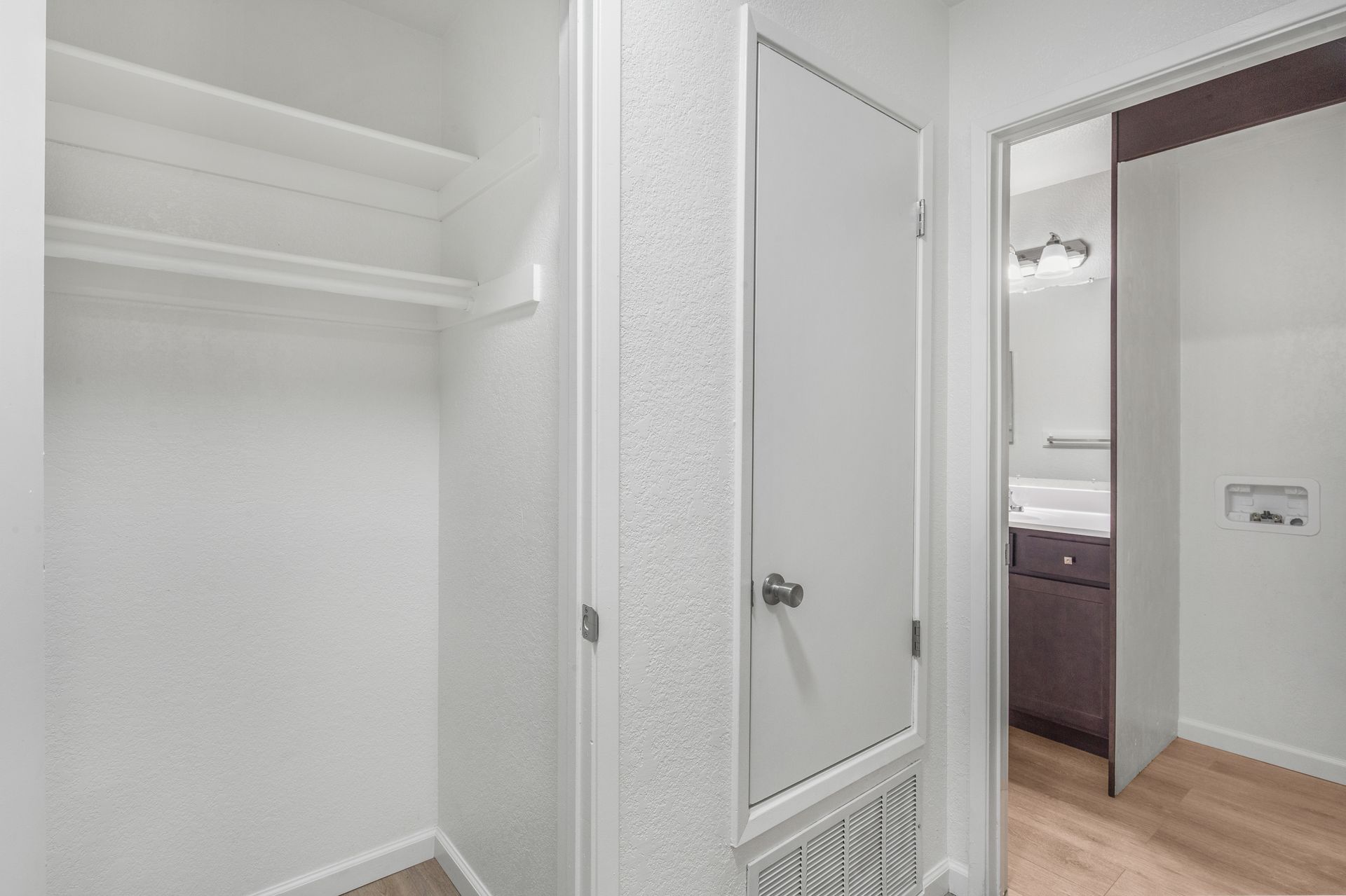 Empty white closet with a door leading to a bathroom.