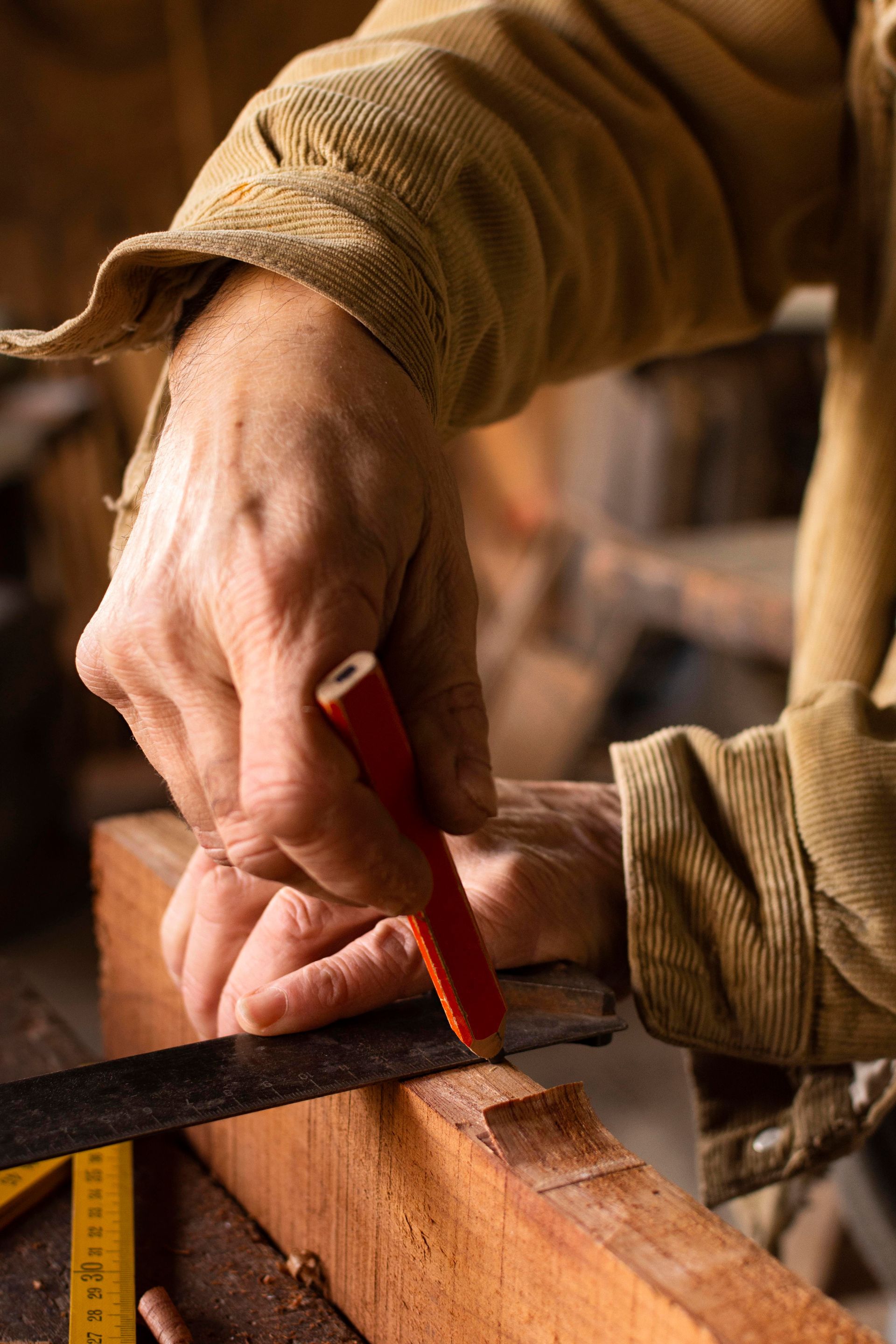 Close-up of a carpenter's hands marking measurements on a piece of wood with a pencil and square