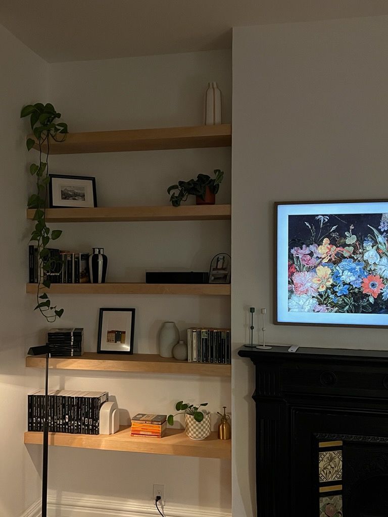 Wooden shelves with plants and objects, beside a fireplace and TV.
