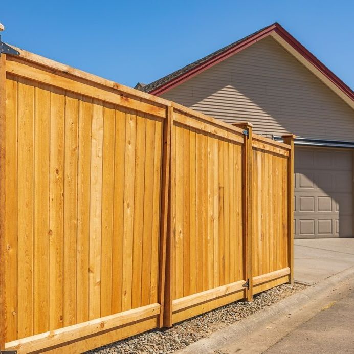 A wooden fence is in front of a house with a garage.