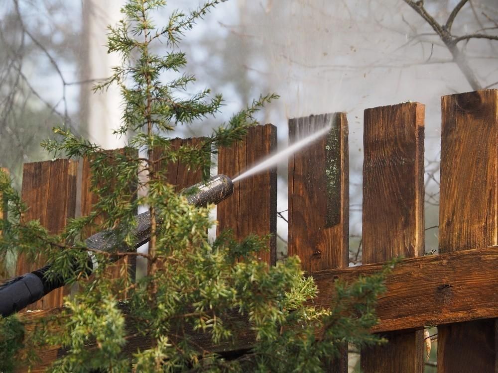 A person is cleaning a wooden fence with a high pressure washer.