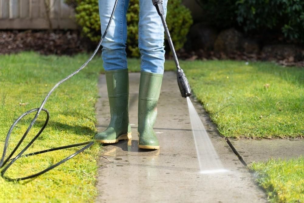 A person is using a high pressure washer to clean a sidewalk.