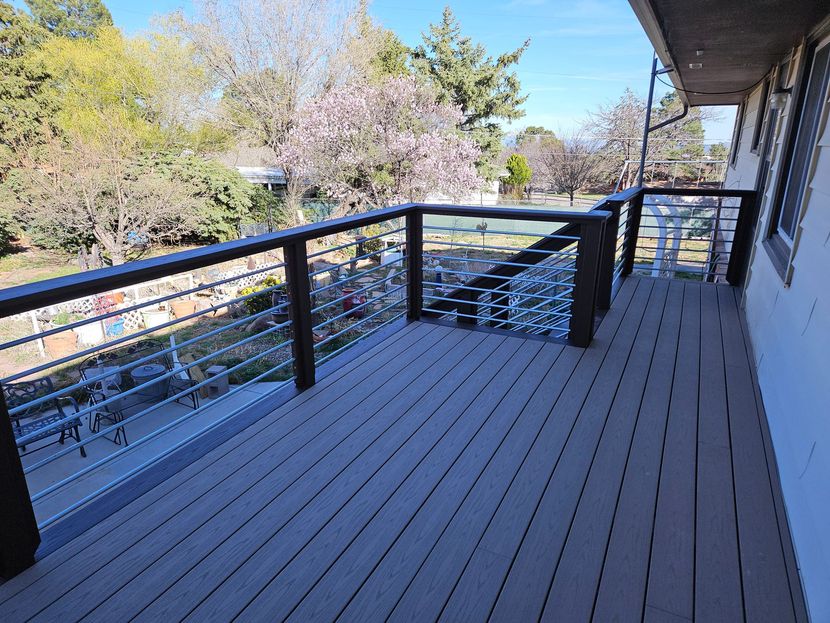 Apartment balcony with black railings, gray deck, and trees in the background.