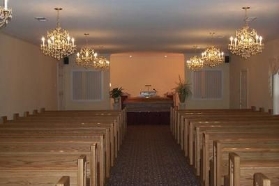 Empty church sanctuary with rows of wooden pews facing a pulpit under four crystal chandeliers.