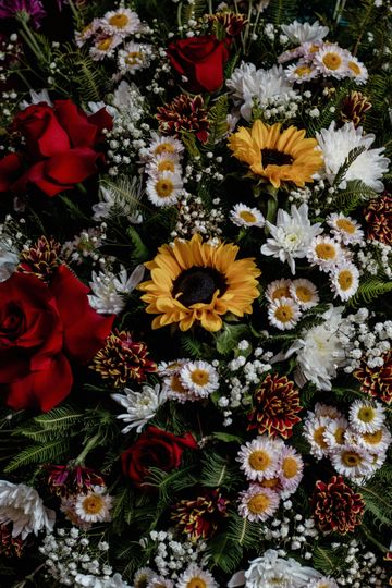 A vibrant floral arrangement featuring red roses, yellow sunflowers, white daisies, and baby's breath.