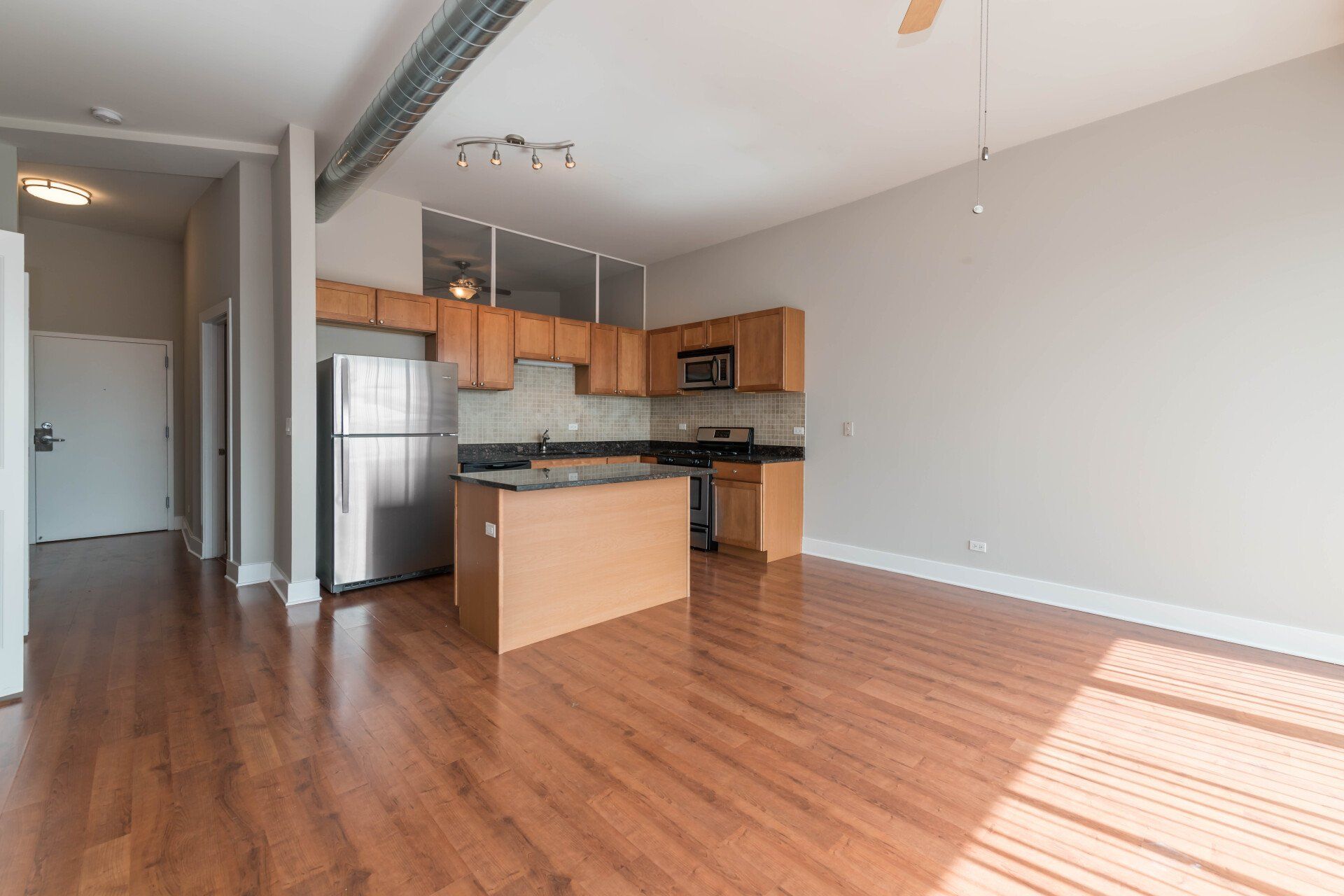 An empty apartment with hardwood floors and a kitchen with stainless steel appliances at 2000 N Milwaukee Apartments.