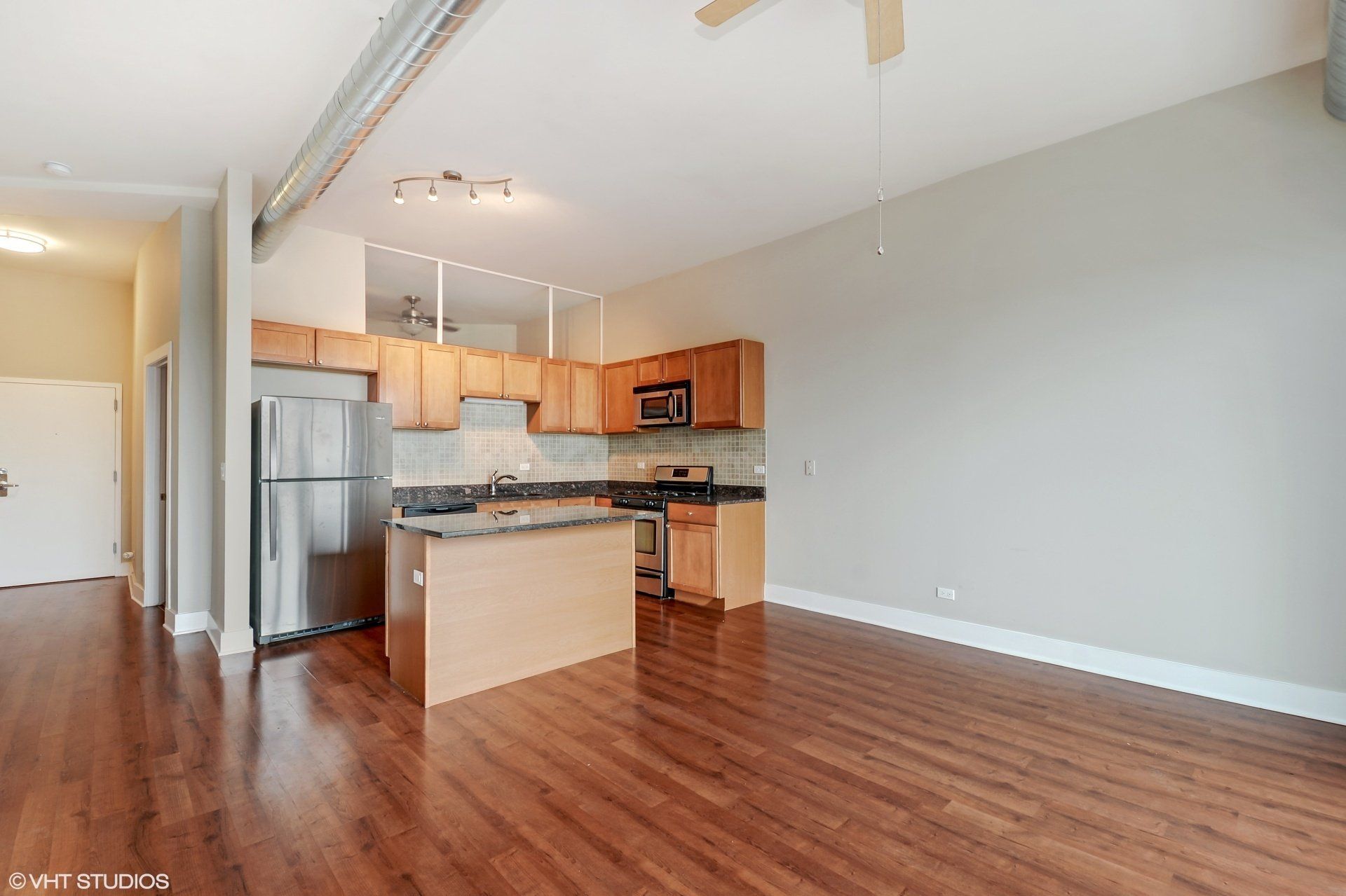 A kitchen with stainless steel appliances and wooden cabinets in an empty apartment at 2000 N Milwaukee Apartments.