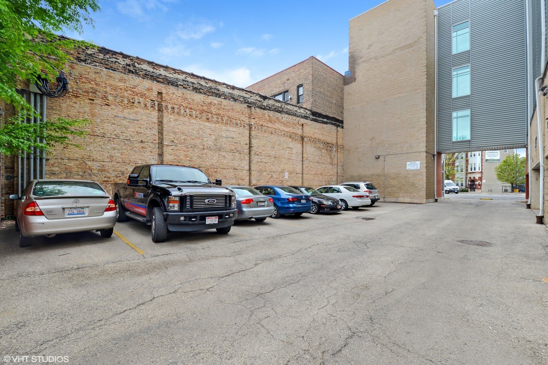 A row of cars are parked in a parking lot next to a building  at 2000 N Milwaukee Apartments.