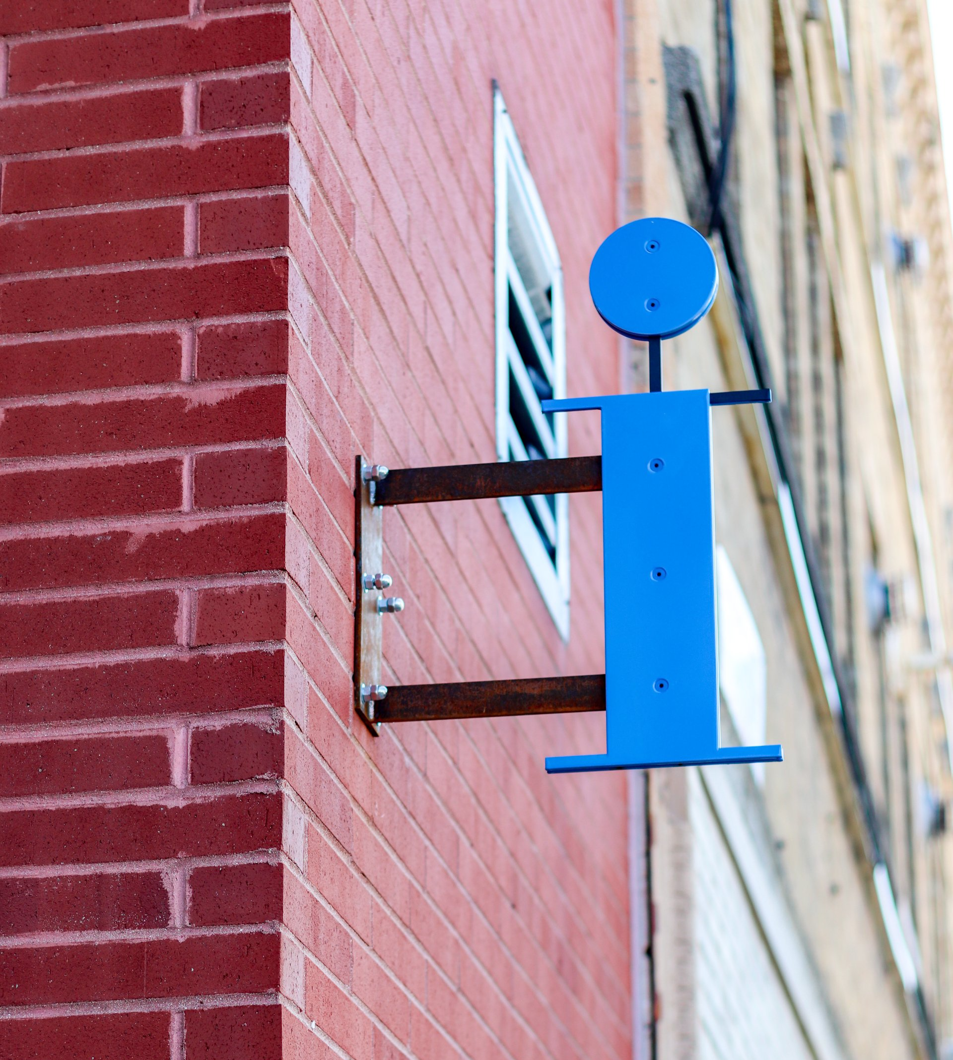 A blue letter i hangs from a red brick wall at 2000 N Milwaukee Apartments.