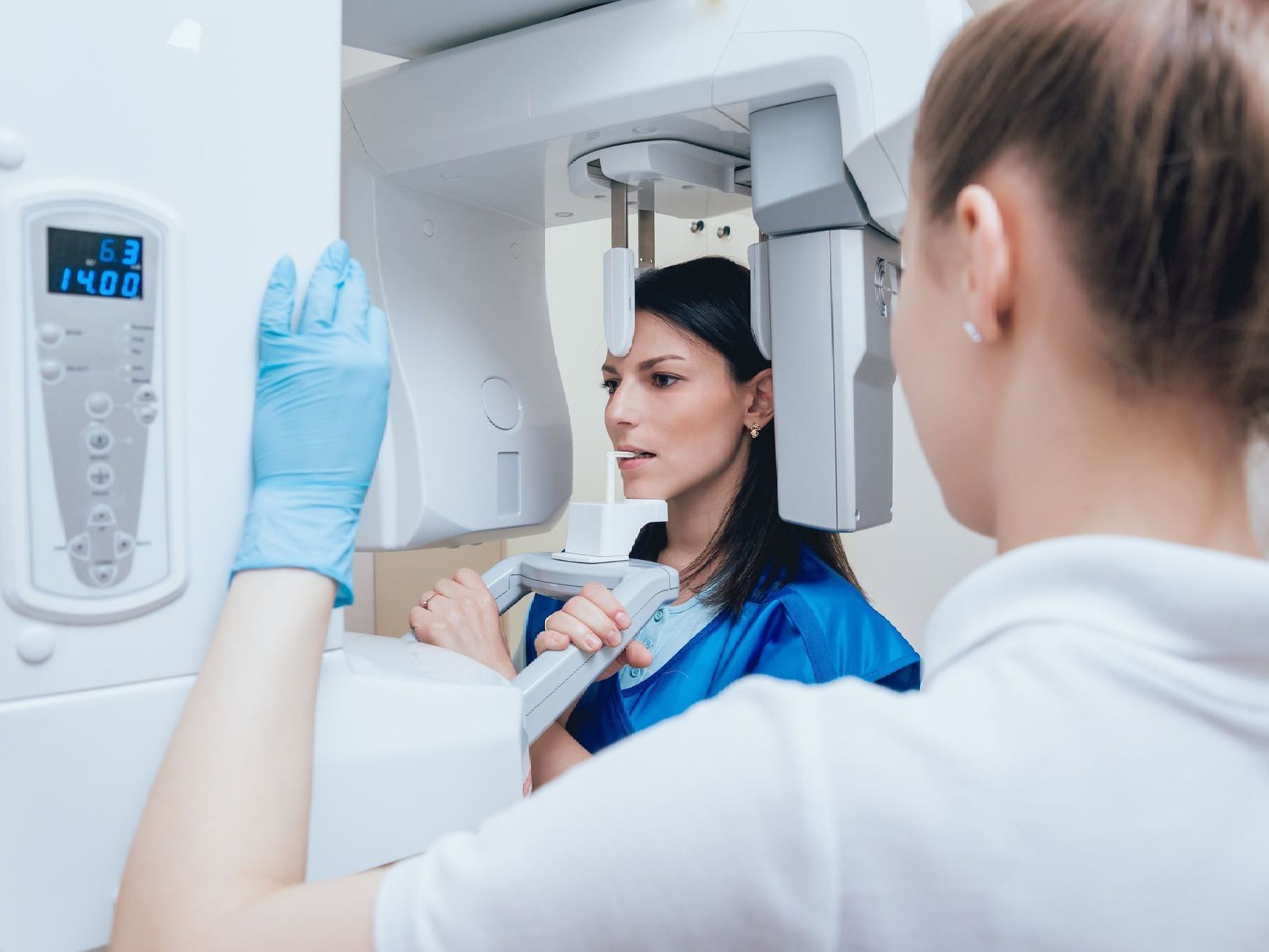 An image of a dental assistant operating a dental x-ray machine with a patient
