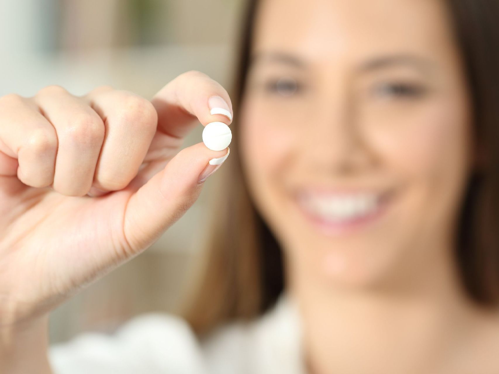 An image of a young woman holding a round pill