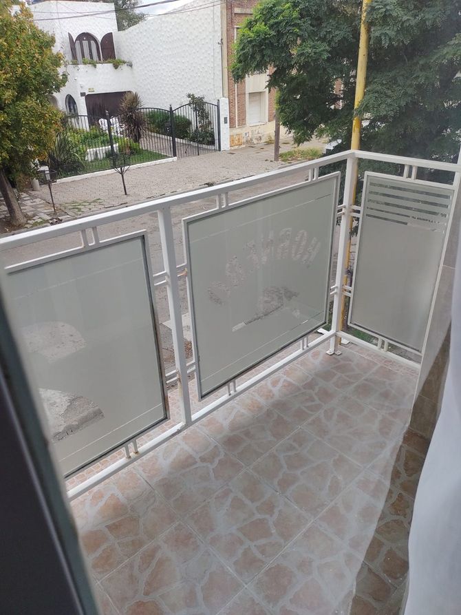 Balcón con estructura de metal blanco y paneles de vidrio esmerilado, con vista a la calle.