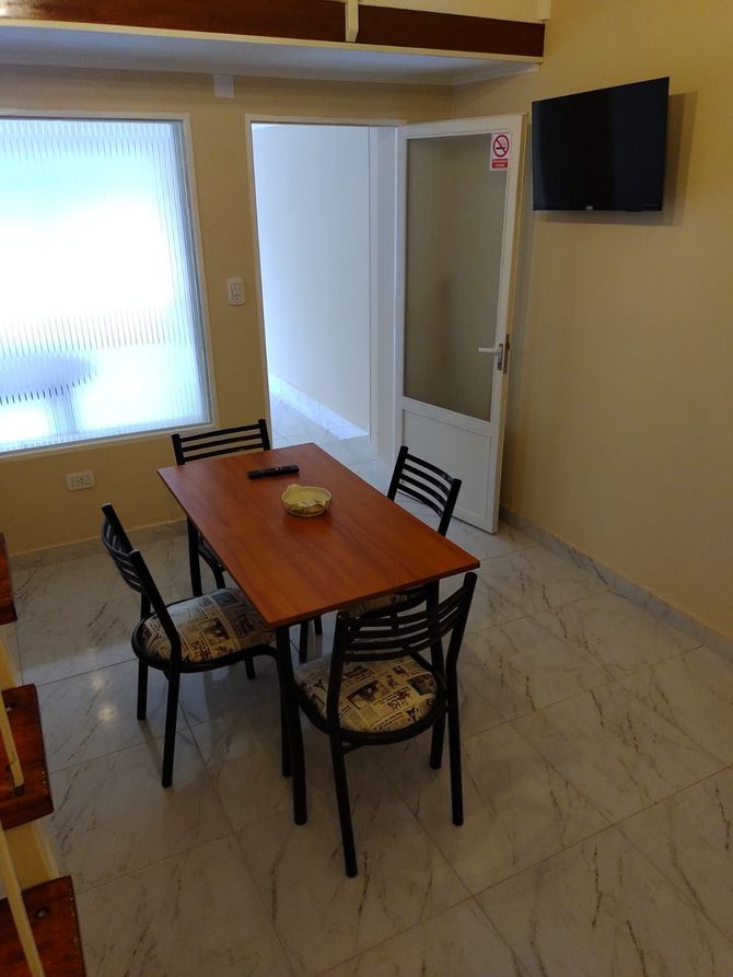 Comedor con mesa, cuatro sillas, TV en la pared, puerta y ventana.