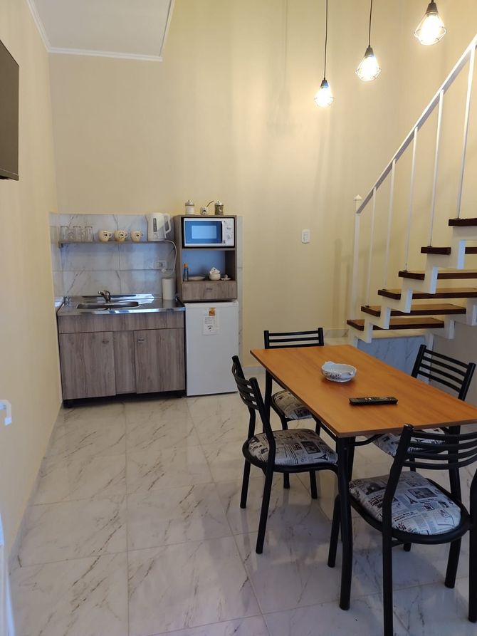 Pequeño apartamento con cocina y comedor, con muebles de madera, mesa y sillas, y una escalera.