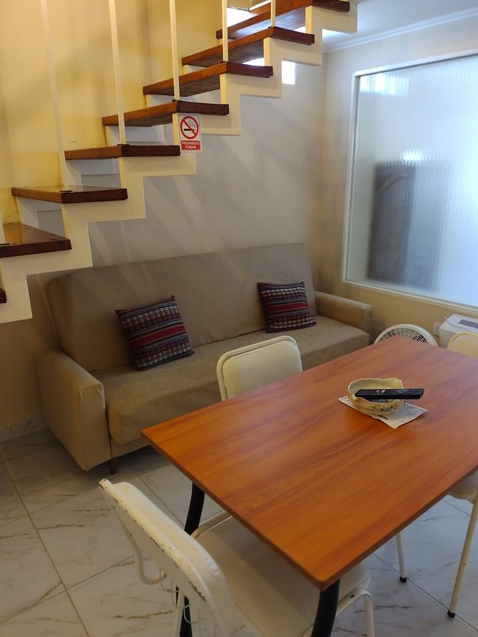 Sala de estar con sofá, mesa y escaleras que conducen hacia arriba.