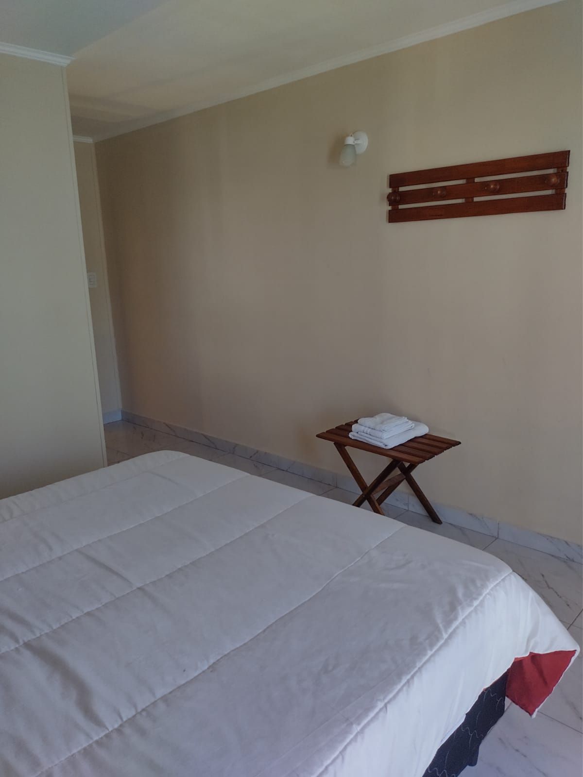 Dormitorio con cama, pequeña mesa de madera con toallas y decoración de madera montada en la pared.