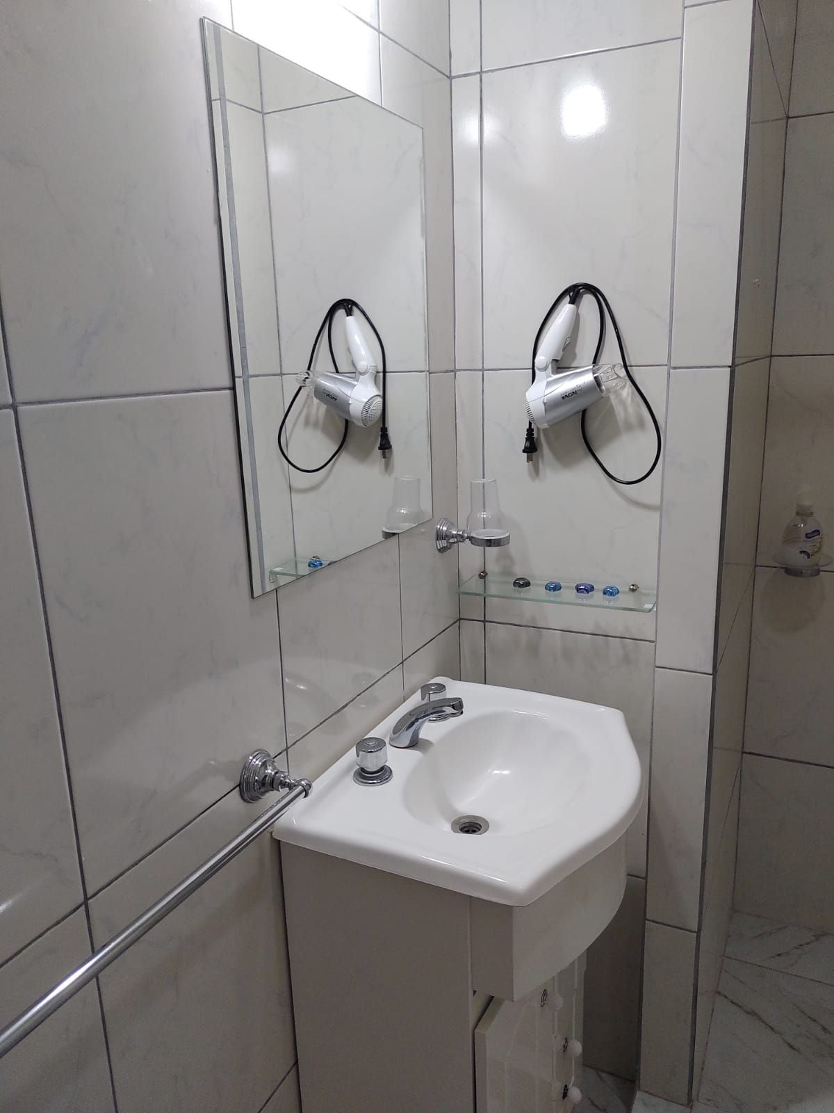 Pequeño baño con lavabo de esquina, espejo, secador de pelo y paredes de azulejos.