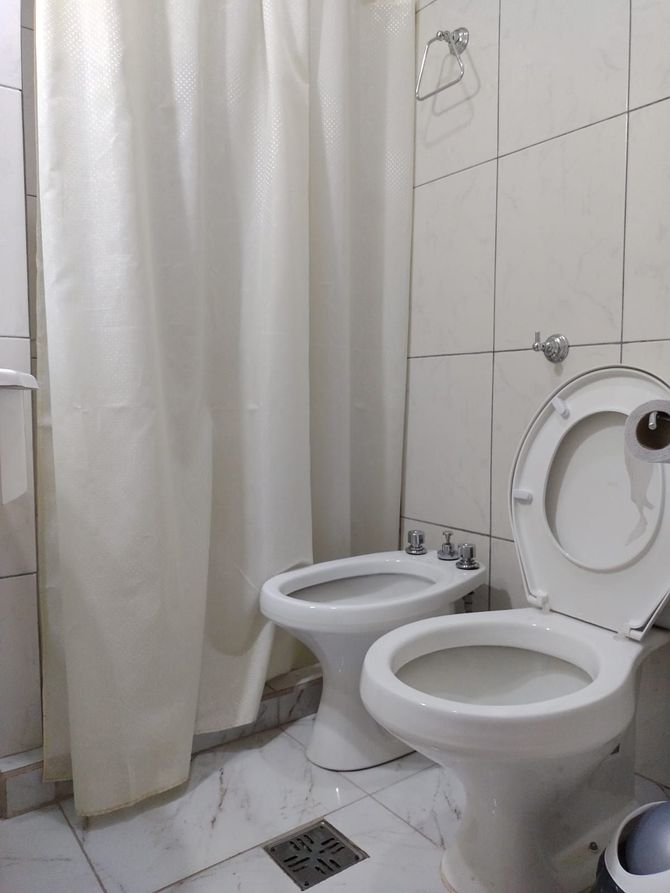 Baño con inodoro blanco, bidet, cortina de ducha y paredes alicatadas.