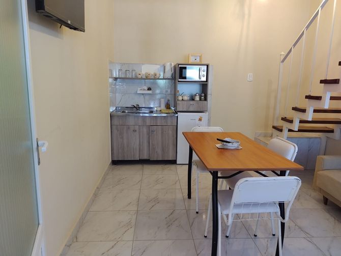 Pequeña cocina y comedor con mesa, sillas y electrodomésticos.