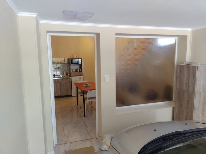 Vista interior: cocina visible a través de la puerta, junto a una ventana esmerilada. Se ve parcialmente un coche en primer plano.