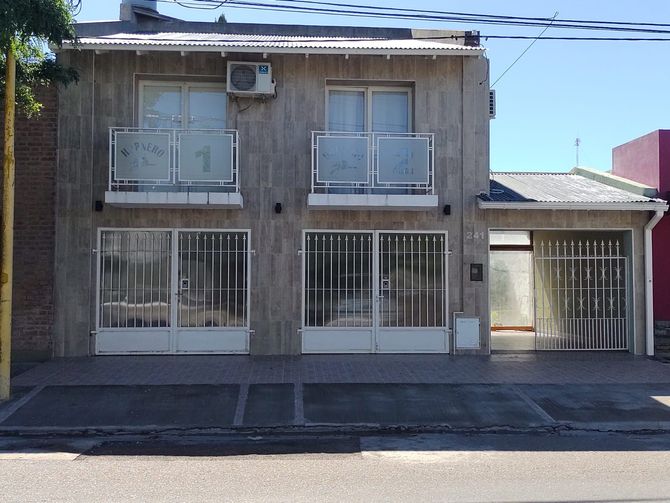 Casa gris de dos pisos con molduras blancas, balcones y puertas de vidrio, ubicada en una calle pavimentada.