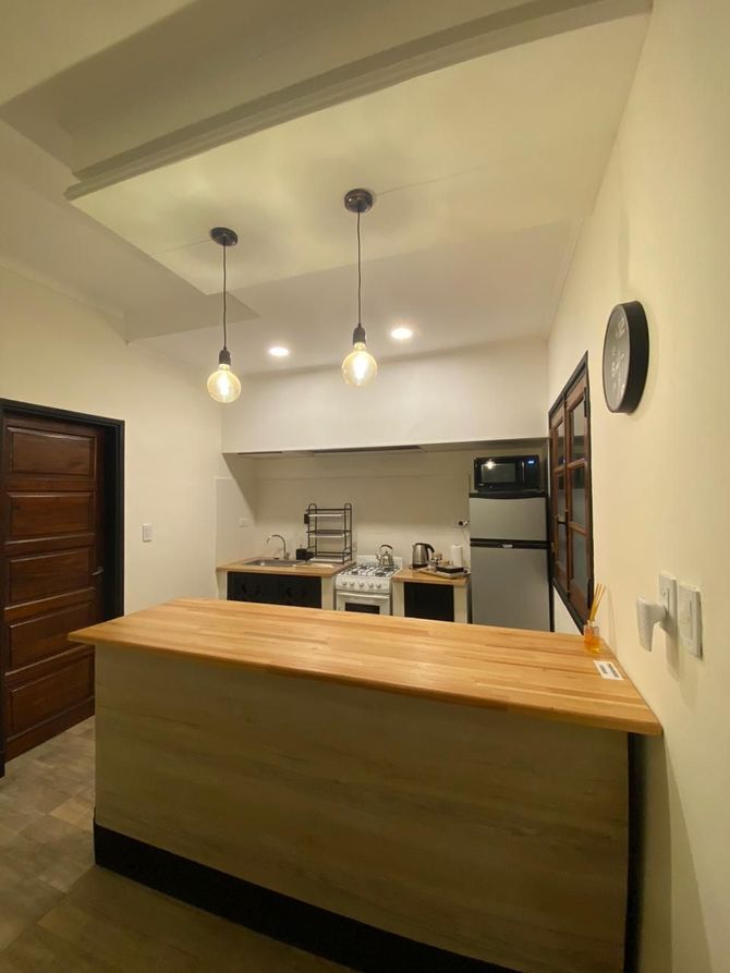 Pequeña cocina con barra de madera, artefactos de iluminación y electrodomésticos.