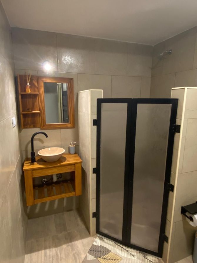 Baño con tocador de madera, lavabo redondo, grifería negra y puertas de ducha de vidrio esmerilado.