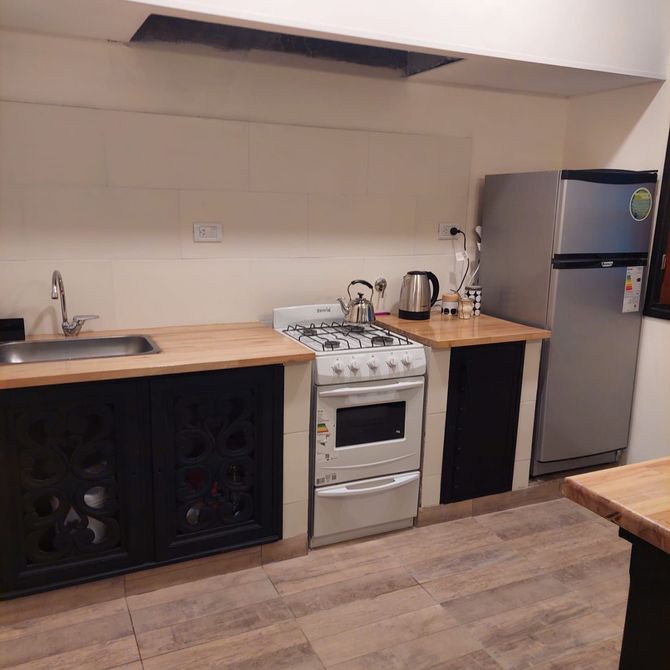 Cocina con gabinetes negros, encimeras de madera clara y refrigerador de acero inoxidable.