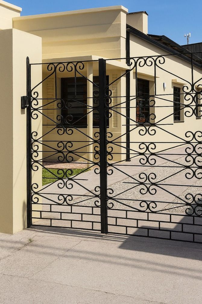 Puerta de hierro forjado negro frente a una casa de estuco amarillo.