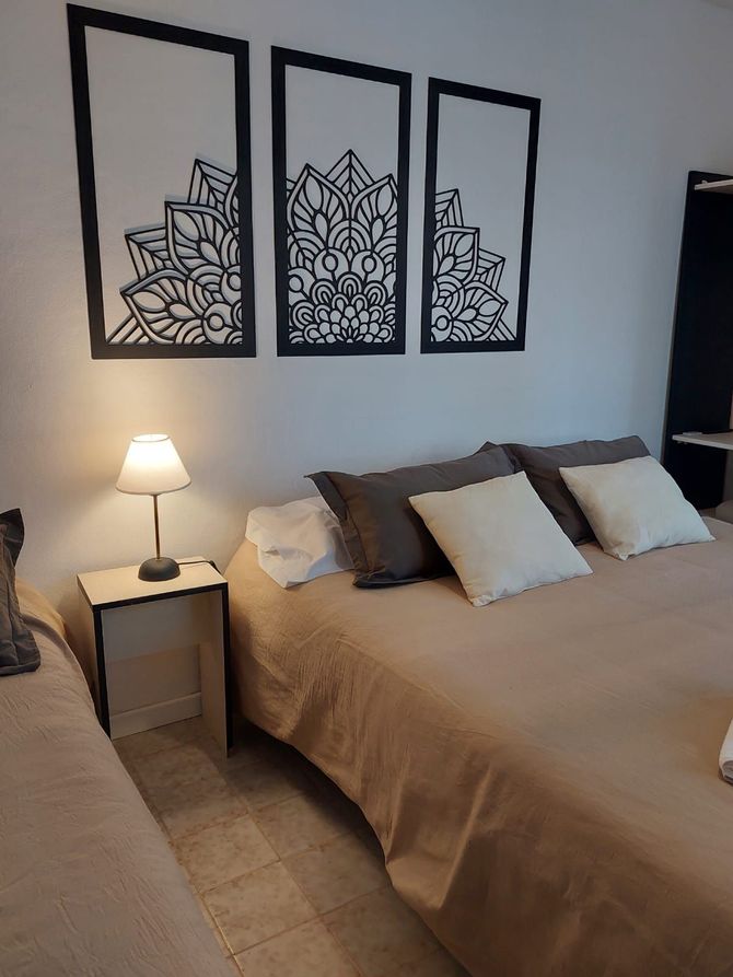 Dormitorio con cama, mesita de noche con lámpara y arte decorativo de pared; tonos neutros.