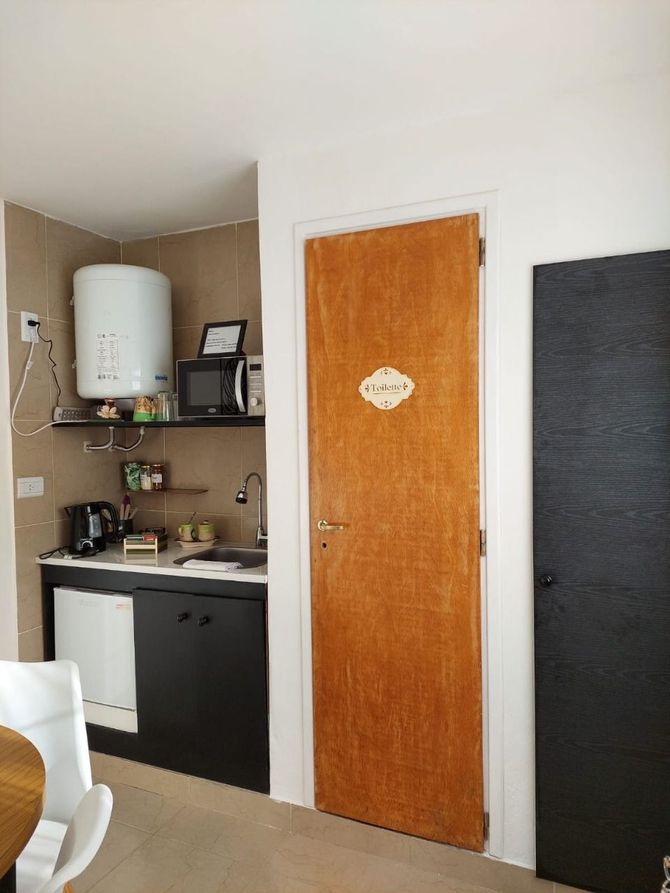 Pequeña cocina con gabinetes negros, puerta marrón y calentador de agua blanco.