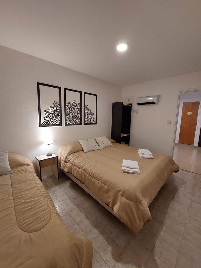 Dormitorio con dos camas, tonos neutros, obra de arte sobre la cama más grande y una puerta.