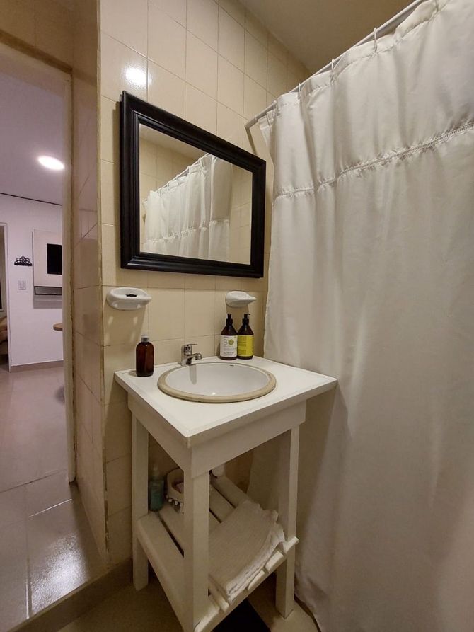 Baño pequeño con lavabo blanco y espejo con marco negro. A la derecha hay una cortina de ducha.