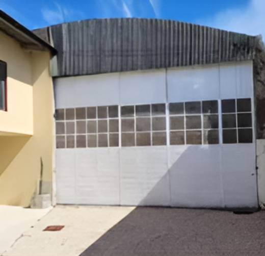 Puerta de garaje blanca con ventanas bajo un techo corrugado, al lado de un edificio amarillo.