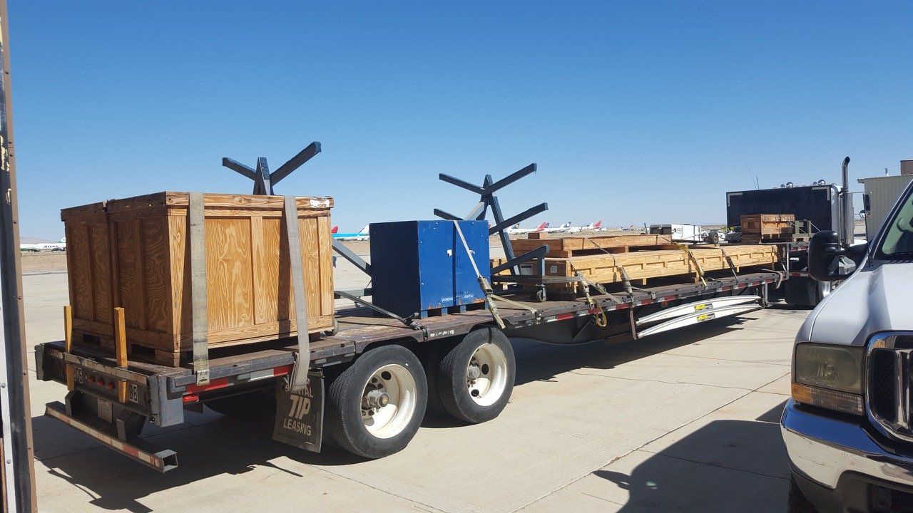 Truck with flatbed trailer carrying wooden crates and beams under a blue sky.