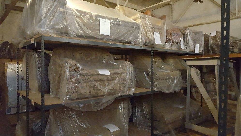 Shelves in a storage room filled with wrapped furniture: chairs and sofas.