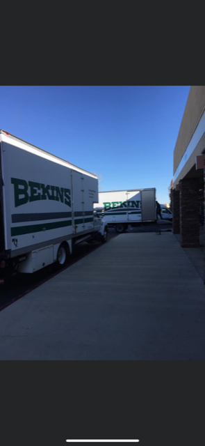 Bekins moving trucks parked at a building dock under a blue sky.