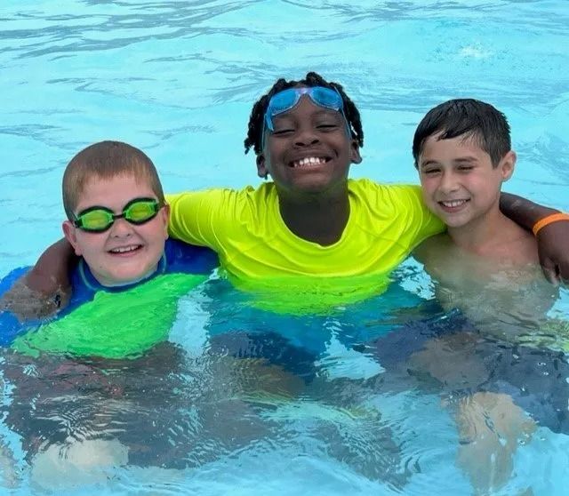Three young boys are posing for a picture in a swimming pool.