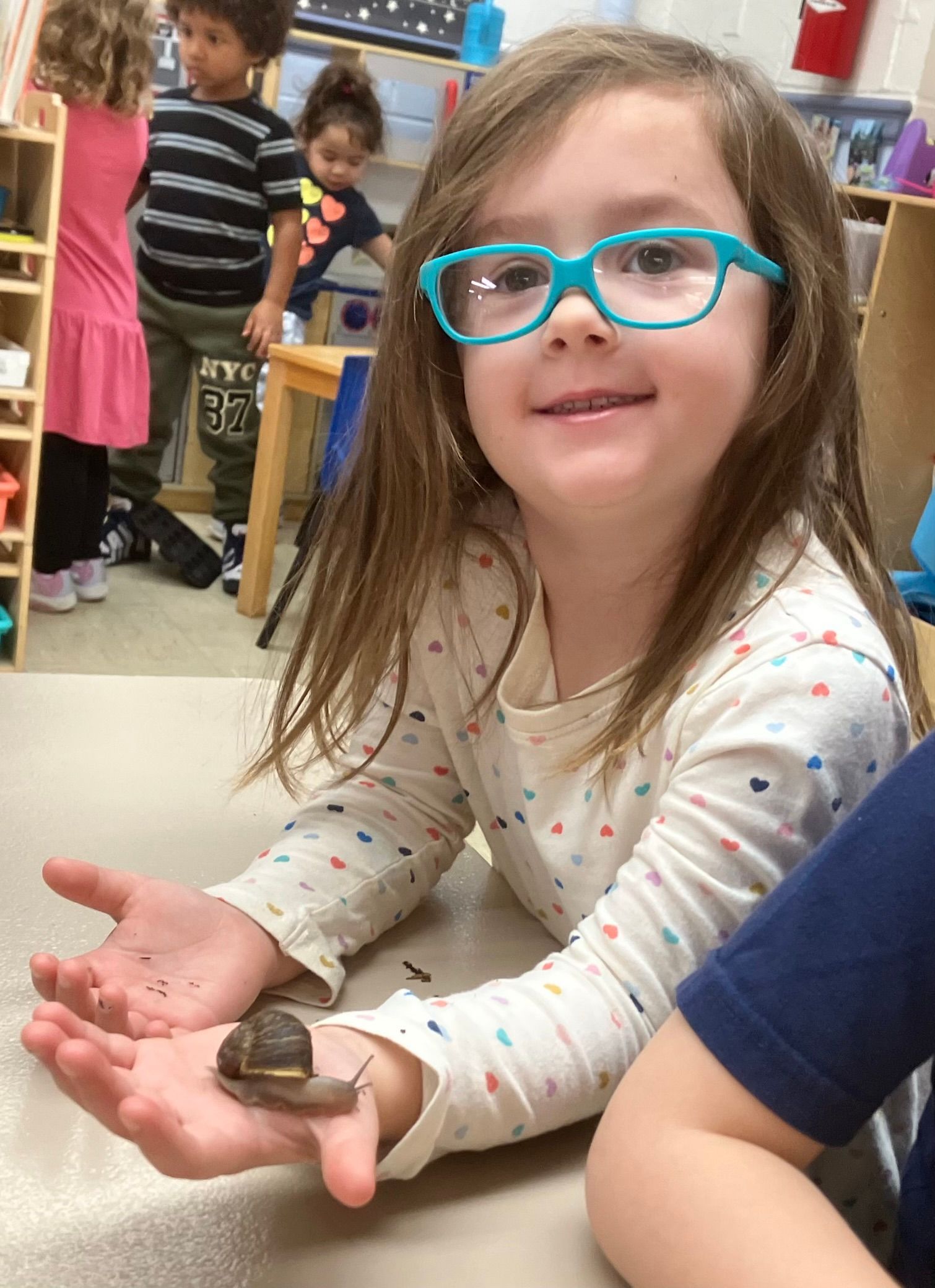 A little girl wearing glasses is holding a snail in her hands.