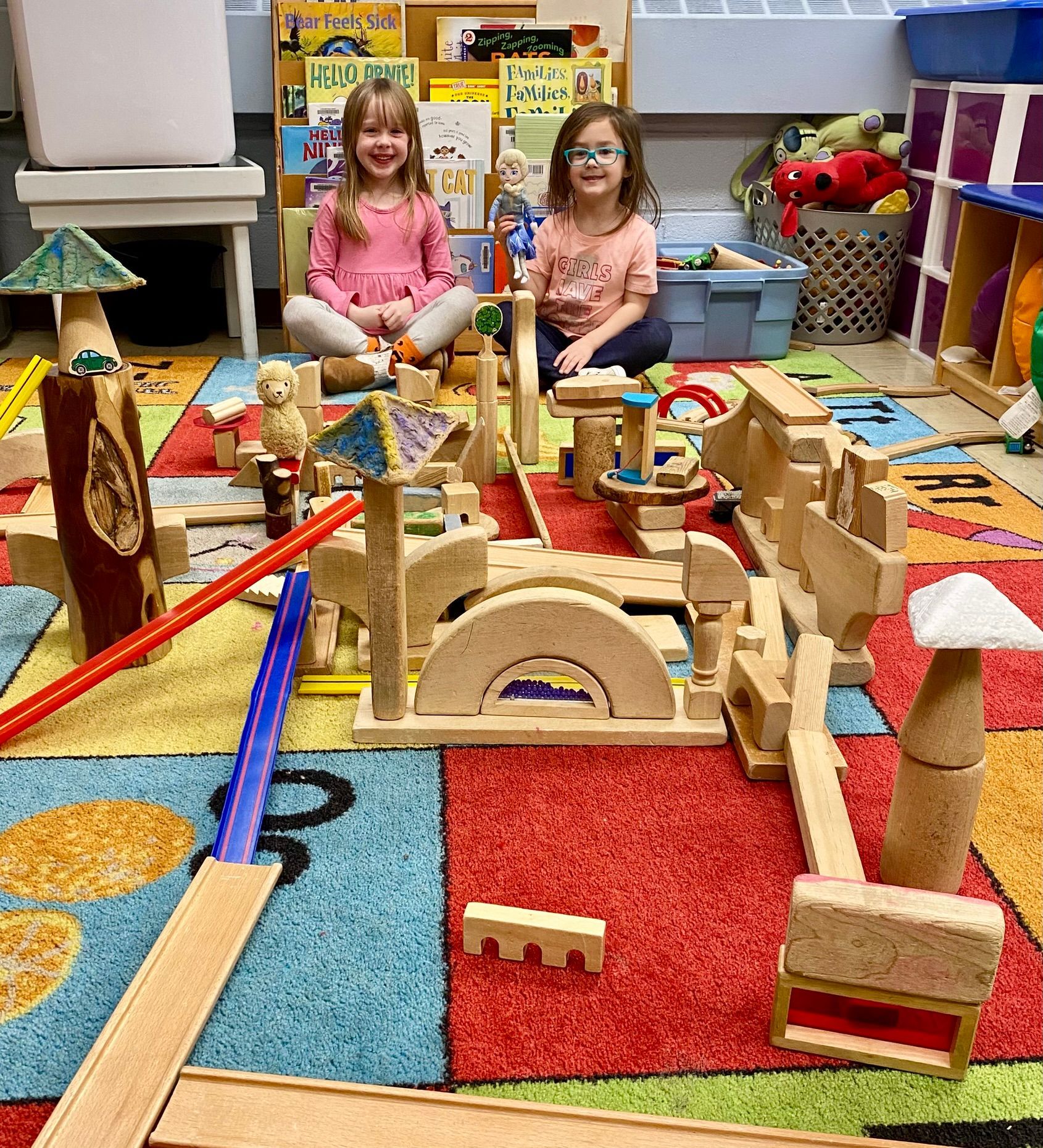 Two young girls are sitting on the floor playing with wooden blocks.