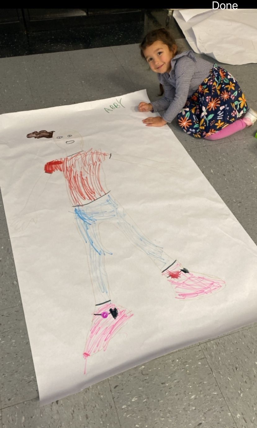 A little girl is sitting on the floor drawing on a large piece of paper.